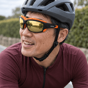Cyclist in a plum jersey and grey helmet wearing black and orange Eyesnug frames with gold lenses.
